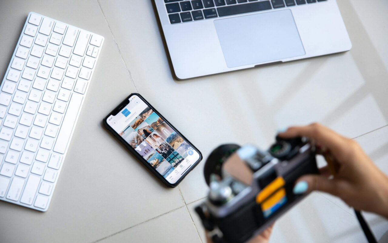 Person using vintage camera with smartphone and laptop in creative setup.